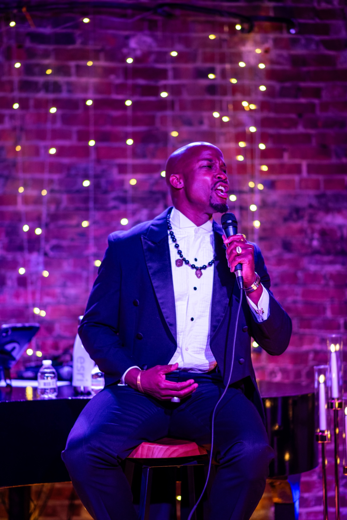 Elias Hendricks seated on stage singing, string lights behind him