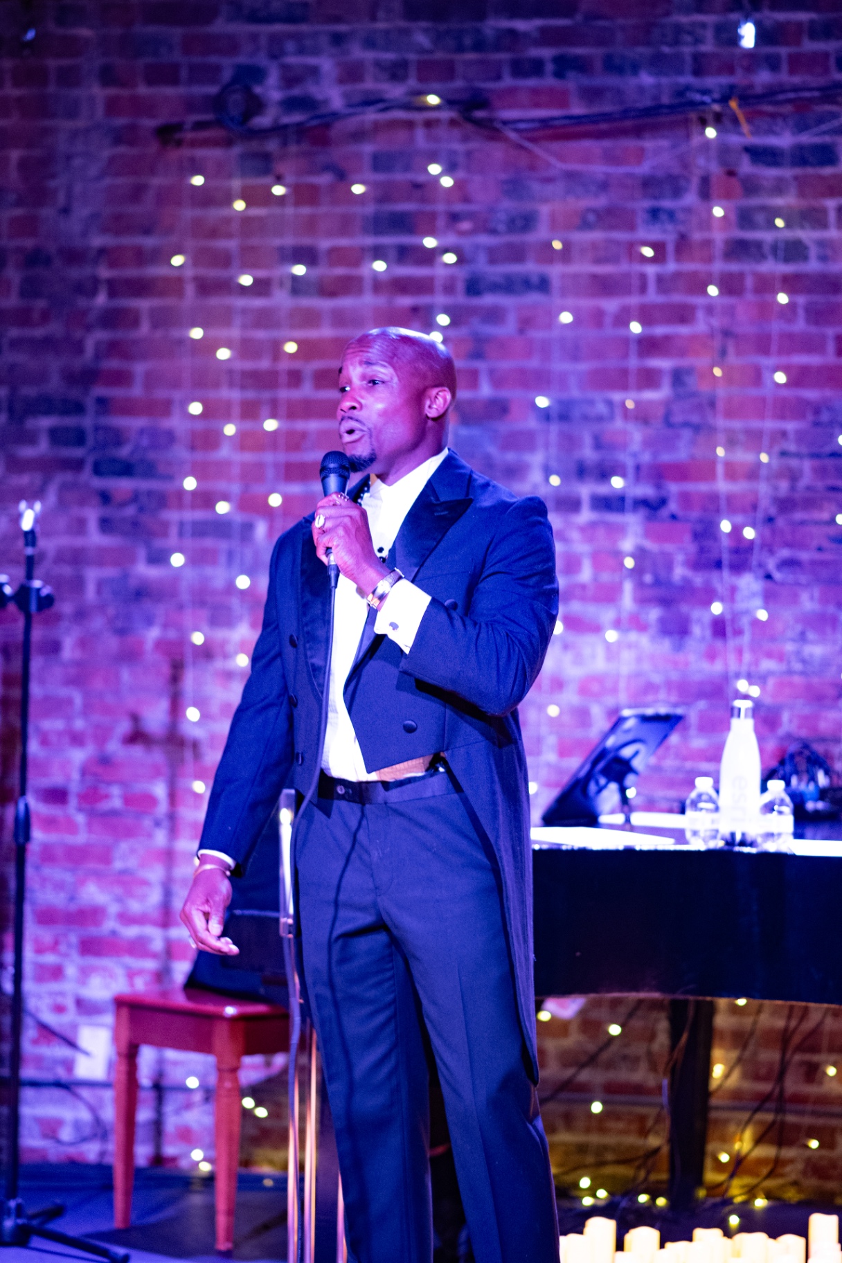 Elias Hendricks singing at the microphone in a tailcoat, candles at his feet