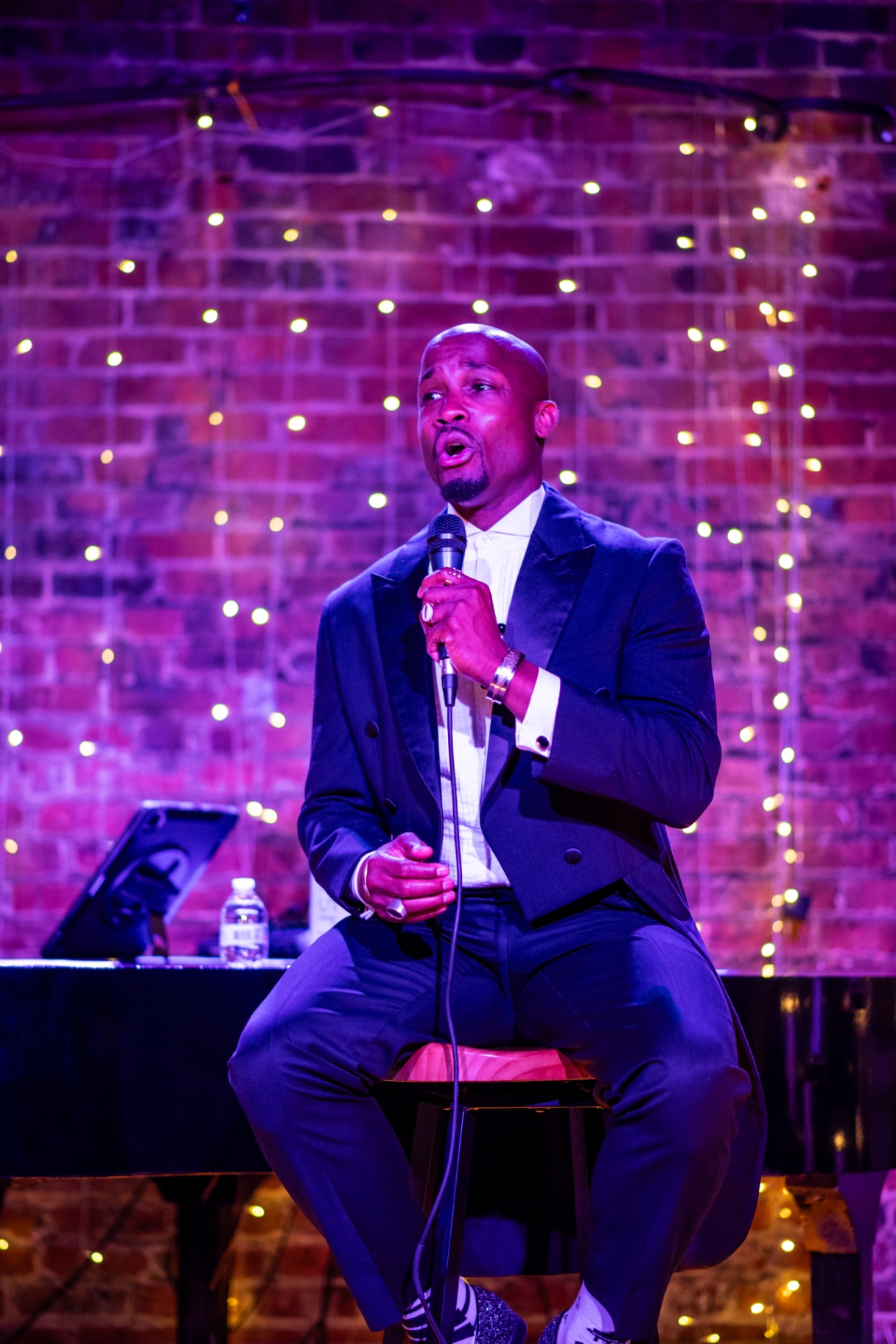 Elias Hendricks seated on a stool, singing at a candlelit concert