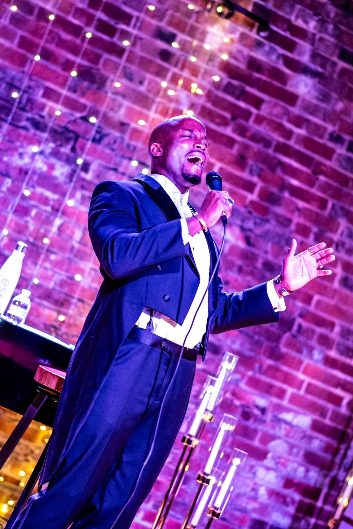 Elias Hendricks with arms open wide, singing under purple stage light