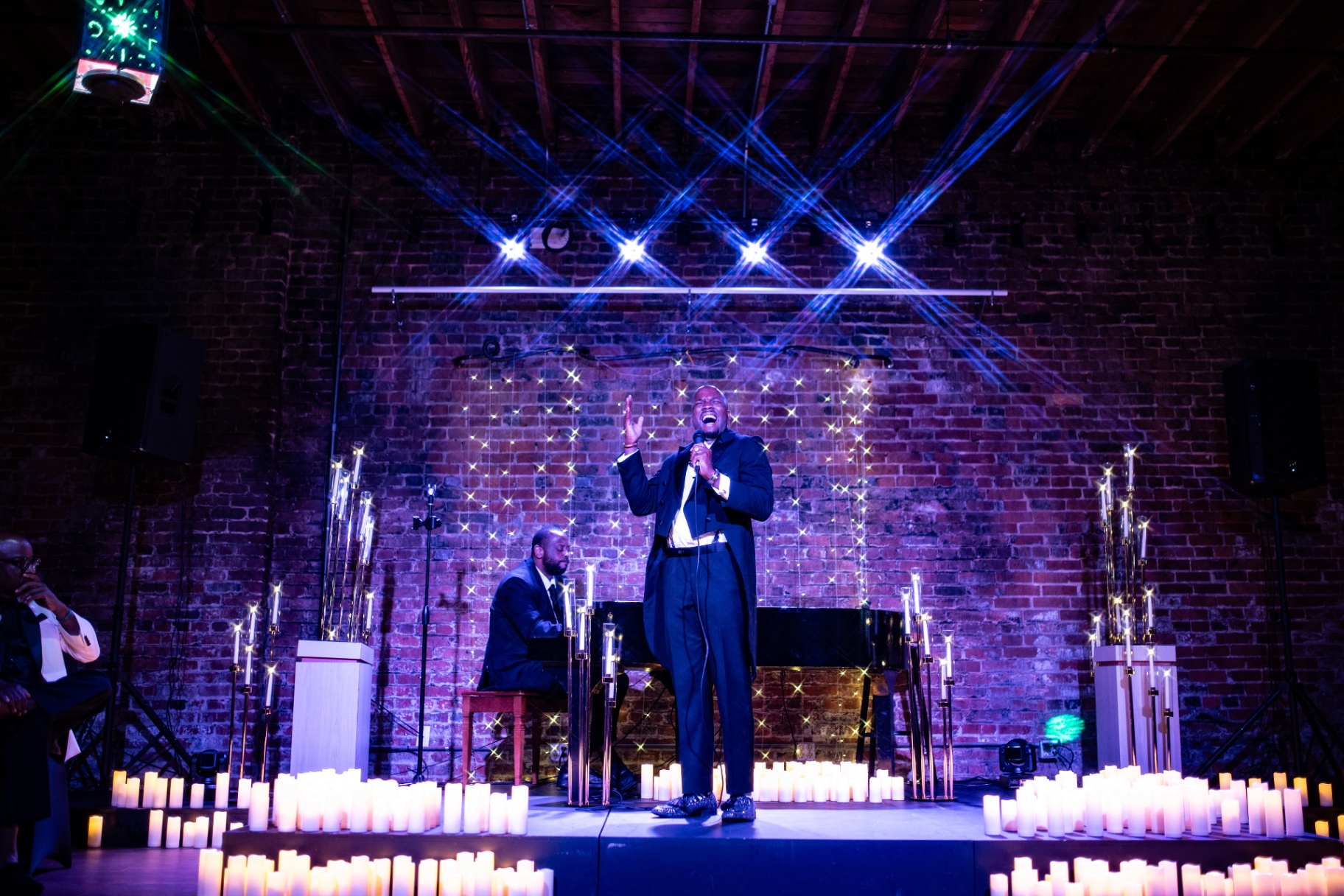 Elias Hendricks singing center stage at a candlelit Classical Soul concert, grand piano and candles behind him